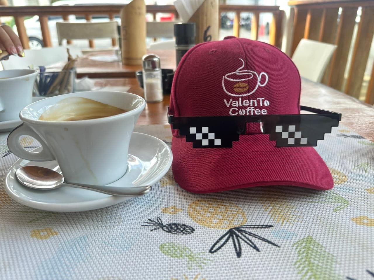 Taza de café ValenTo Coffee junto a la gorra oficial de la marca en una cafetería